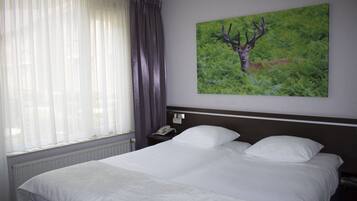 Een hotelkamer met een groot bed, een nachtkastje, een telefoon en een schilderij van een hert op de muur.
