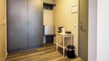 Ein Flur mit Holzboden, einem weißen Tisch mit Wasserkocher und Tassen, einem Mülleimer und einem geschlossenen Kleiderschrank.