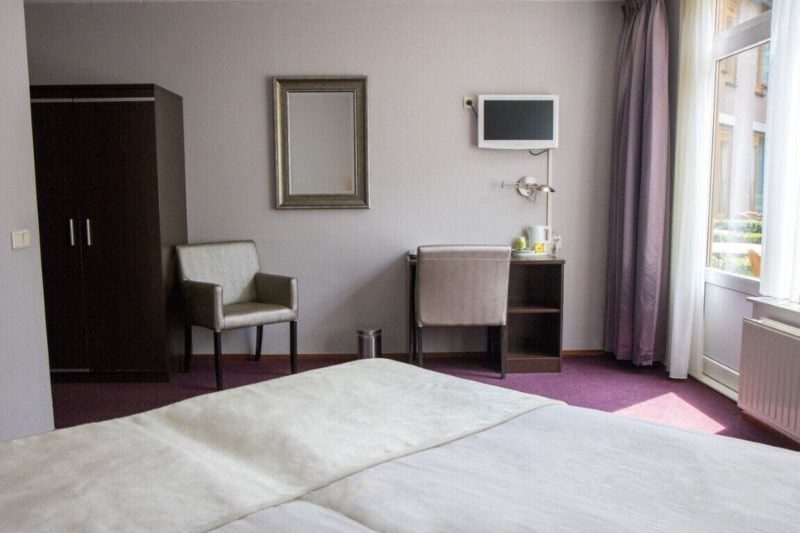 Een hotelkamer met een bed, een stoel, een bureau met een lamp, een televisie en een kledingkast.