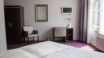 Een hotelkamer met een bed, een stoel, een bureau met een lamp, een televisie en een kledingkast.