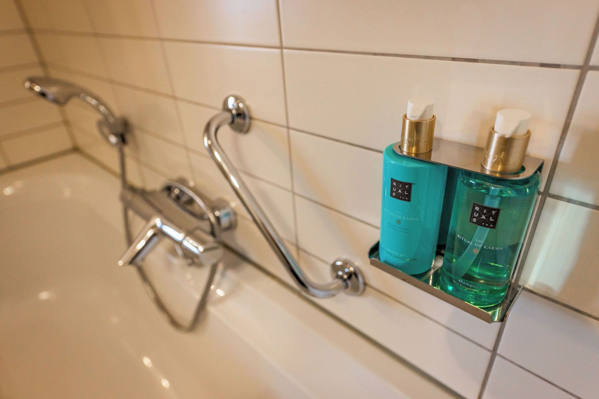 Un baño con ducha, barras de apoyo y dos botellas de champú en un estante.