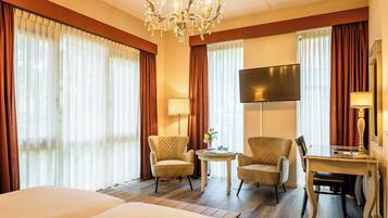 A hotel room with two beds, a desk, two chairs, a TV, and a chandelier.