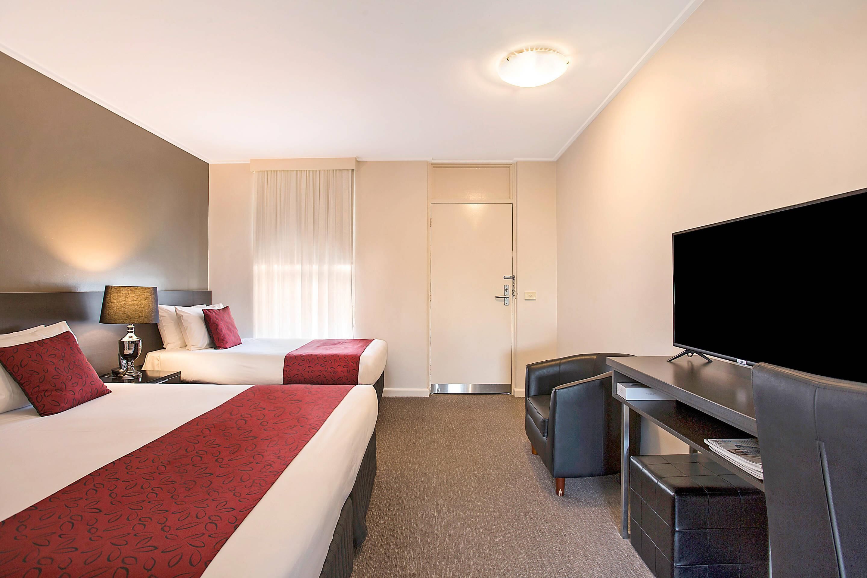 Een hotelkamer met twee bedden, een televisie, een bureau en een raam met gordijnen.