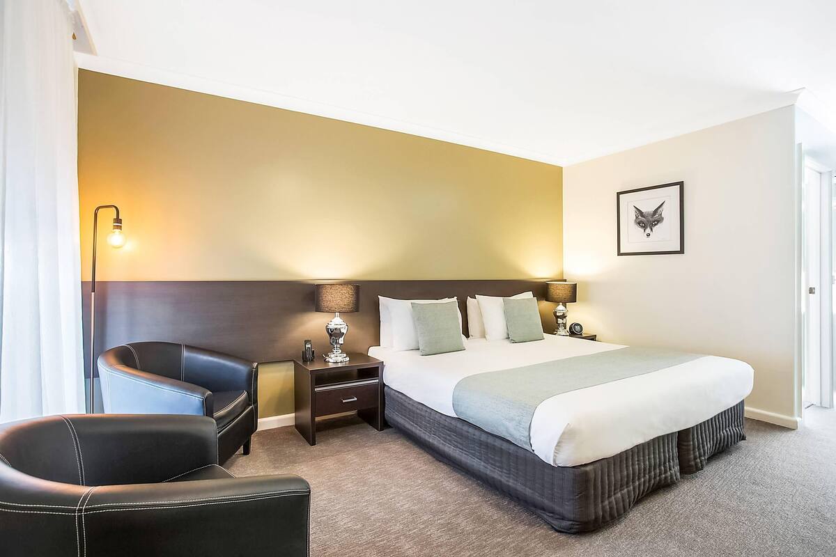 A hotel room with a bed, two bedside tables, a chair, and a lamp.