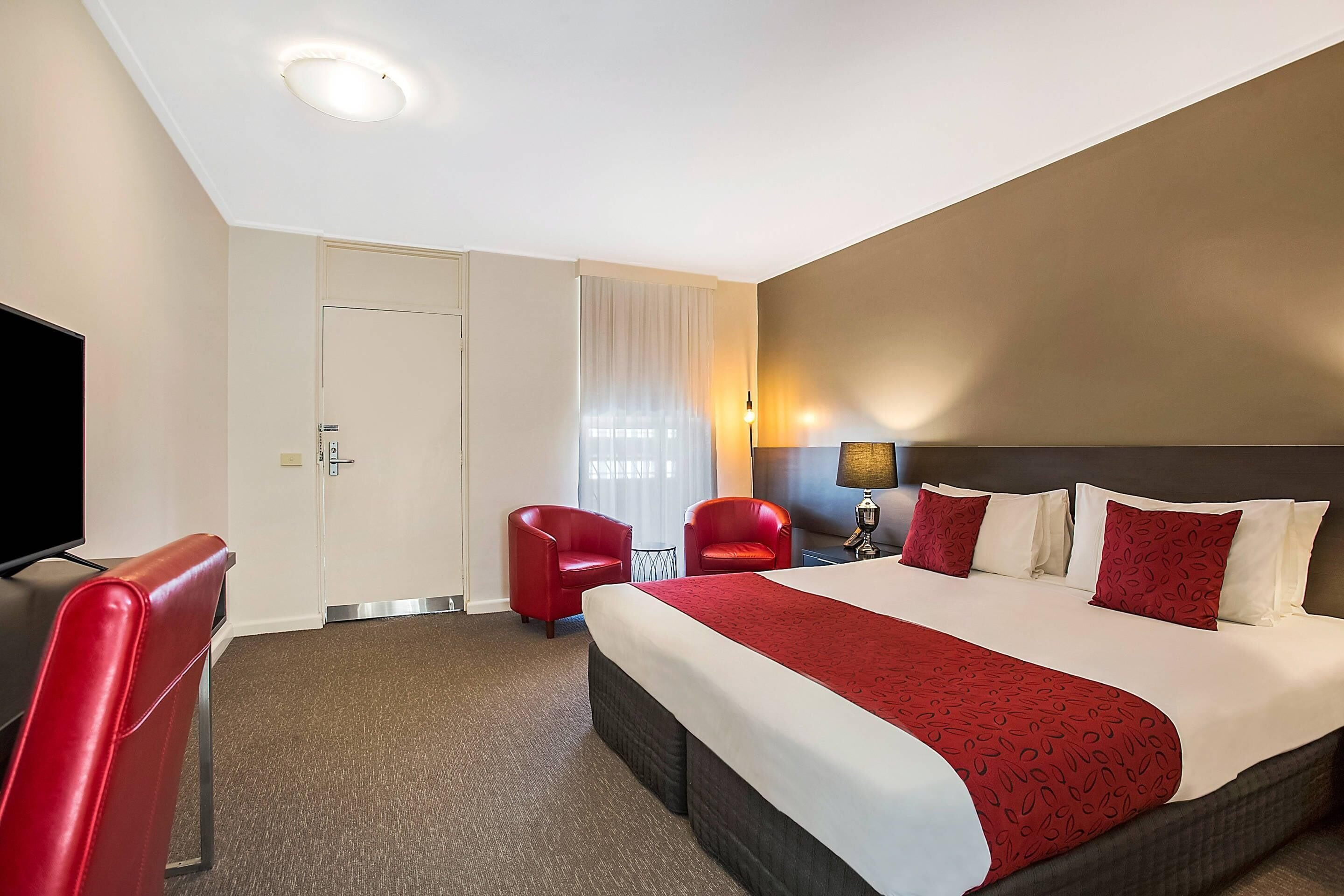 Ein Hotelzimmer mit einem großen Bett, zwei roten Stühlen, einem Fernseher und einer Tür.