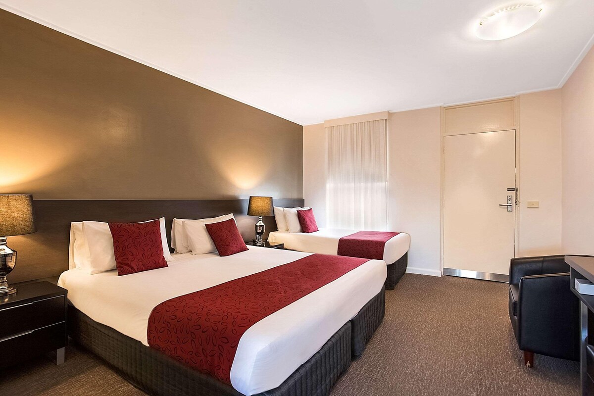 Habitación de hotel con dos camas, un escritorio y una puerta.
