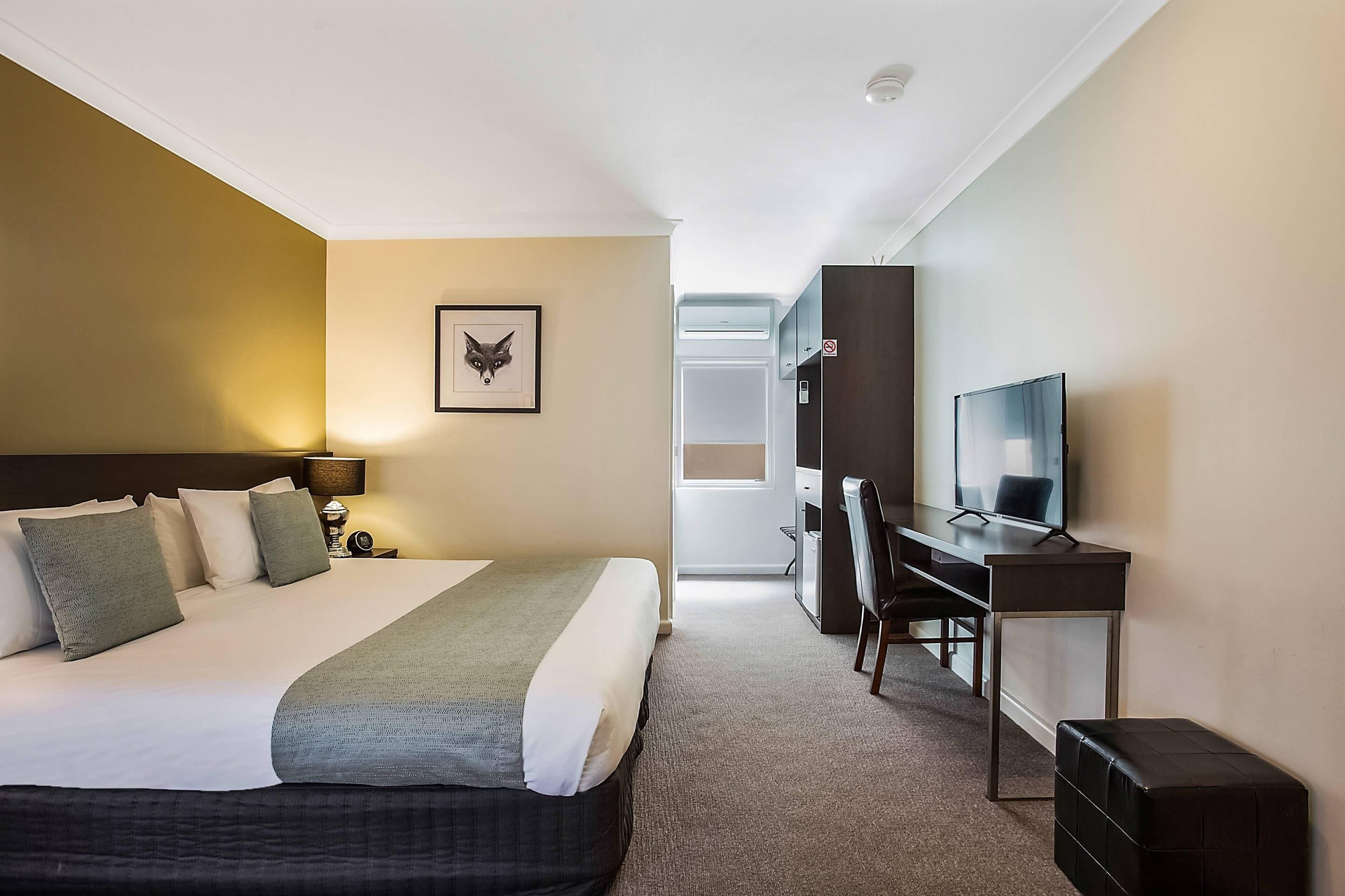 Habitación de hotel con cama, escritorio, televisión y un cuadro en la pared.