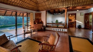A spacious room with a high ceiling, wooden furniture, and large windows offering a view of a lush garden. - Evolve Back, Coorg (Virajpet)