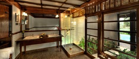 A bathroom with wooden beams, a glass shower enclosure, and a view of greenery outside.