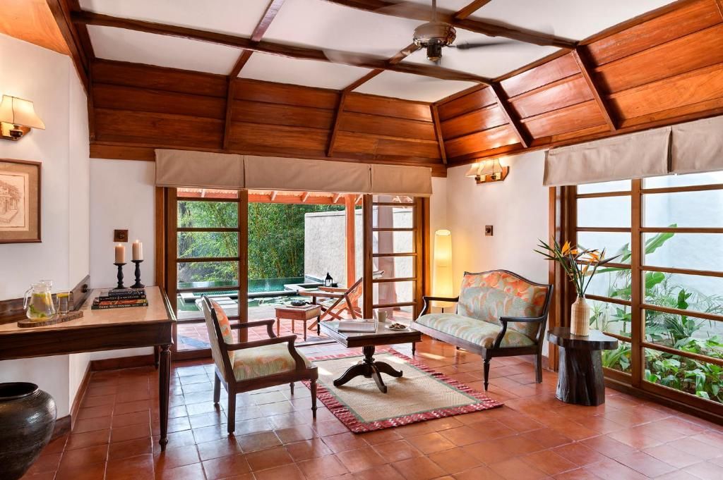 Una habitación con techo de madera, ventanas amplias, un sofá, sillas, una mesa y un jarrón decorativo.