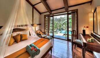 Un dormitorio con cama, una silla, una mesa con velas y vistas a una piscina y jardín.