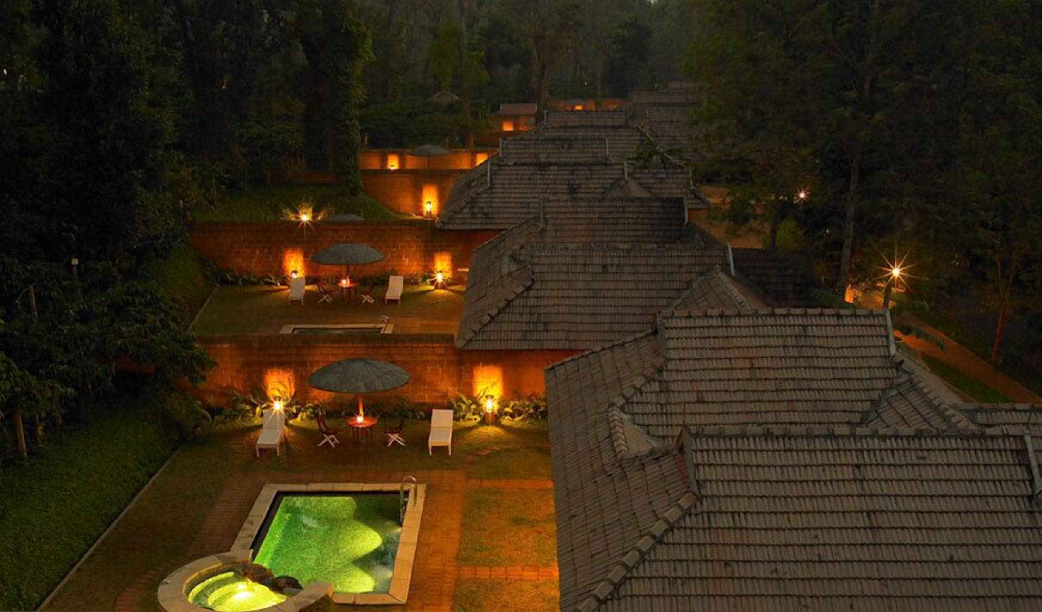 A rooftop pool area with lounge chairs and umbrellas, surrounded by terraced buildings and trees.