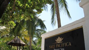 A sign for Sari Pacifica Resort Spa on Lang Tengah Island, surrounded by palm trees and a thatched-roof structure.
