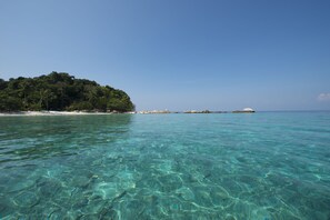 A clear turquoise sea with a sandy beach and a small island with dense vegetation.