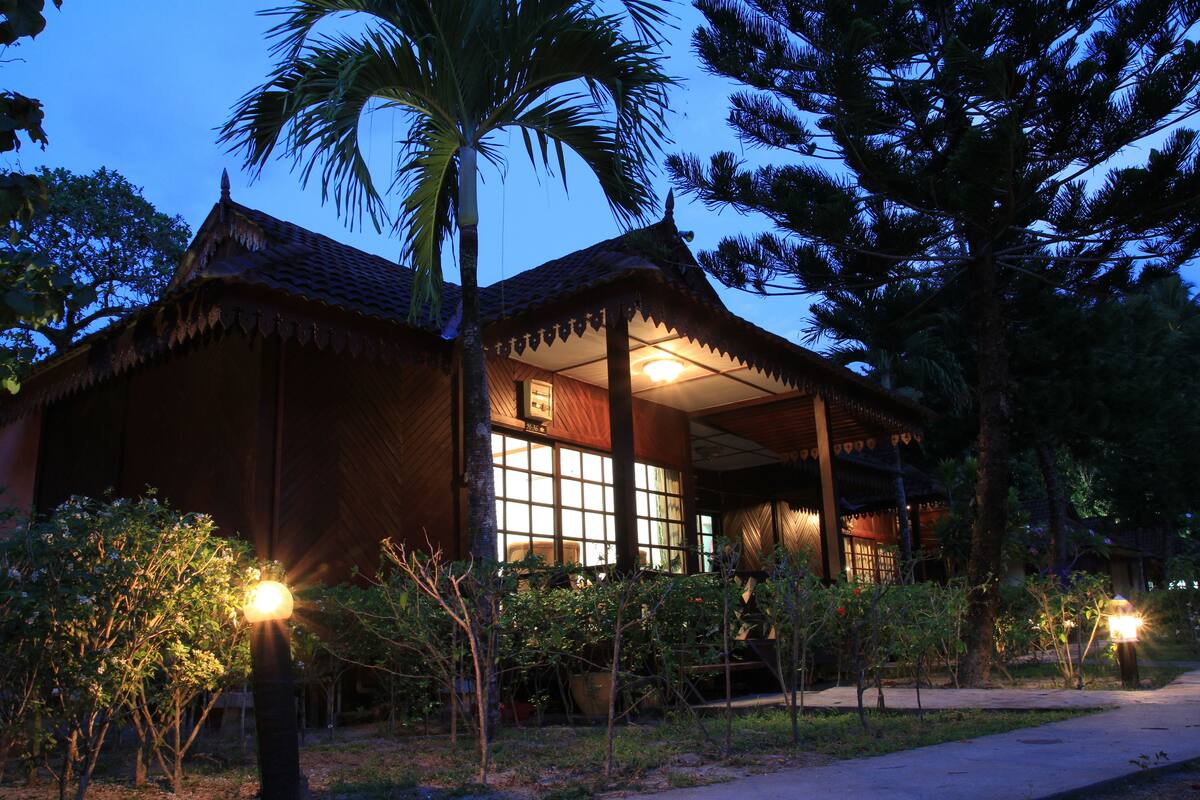 A traditional wooden building with a thatched roof, large windows, and a well-lit entrance.