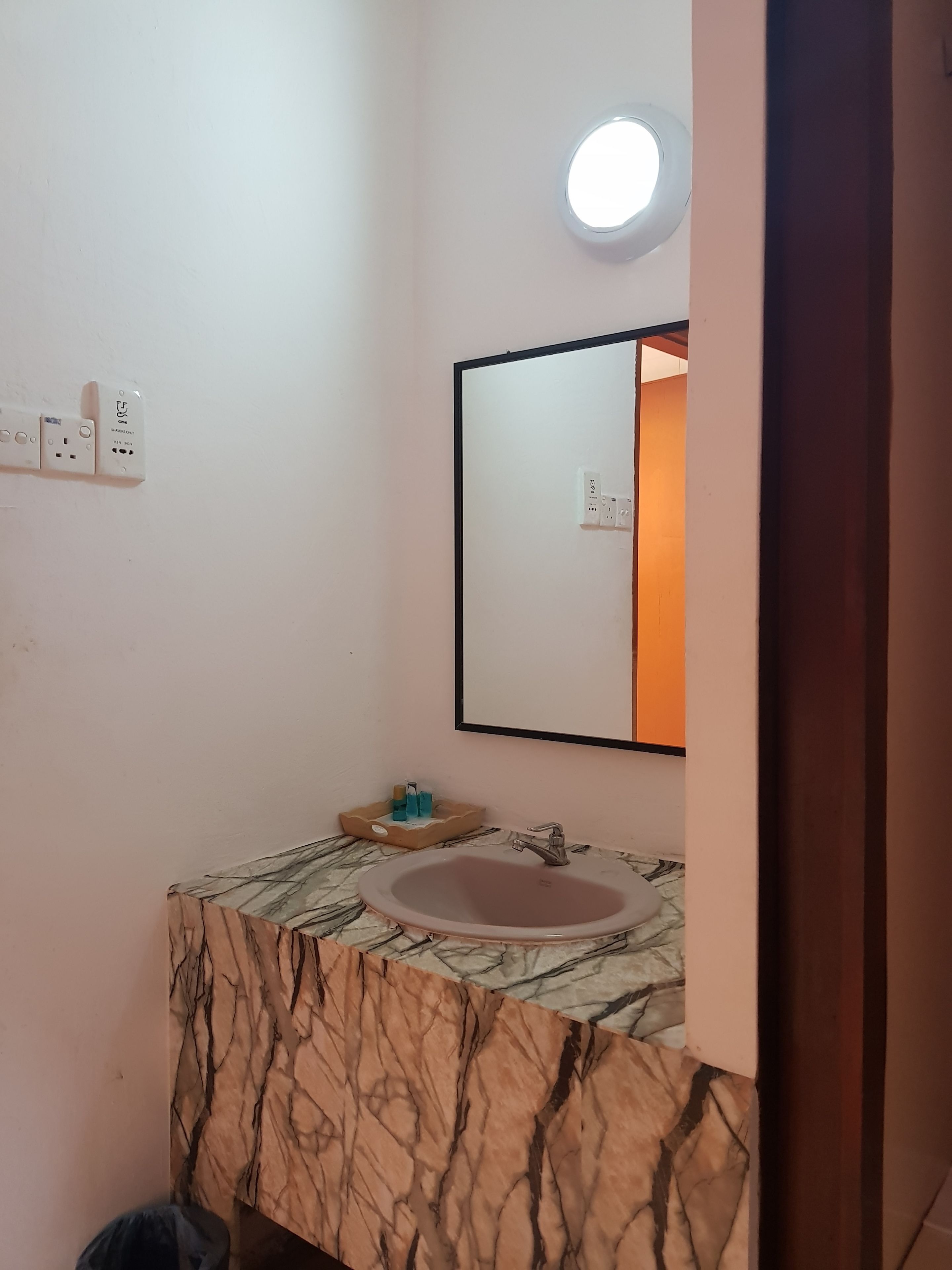 Une salle de bain avec un lavabo en marbre, un miroir et un luminaire placé au-dessus du miroir.