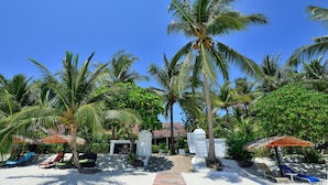 A resort with a sandy beach, palm trees, and lounge chairs.