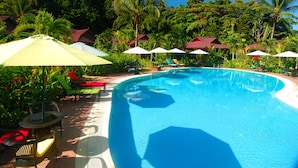 A swimming pool with lounge chairs and umbrellas, surrounded by palm trees and a tropical setting.
