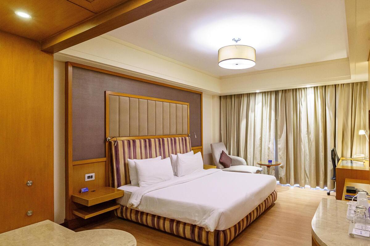 Una habitación de hotel con una cama grande, un escritorio, una silla, una mesita de noche y un baño.