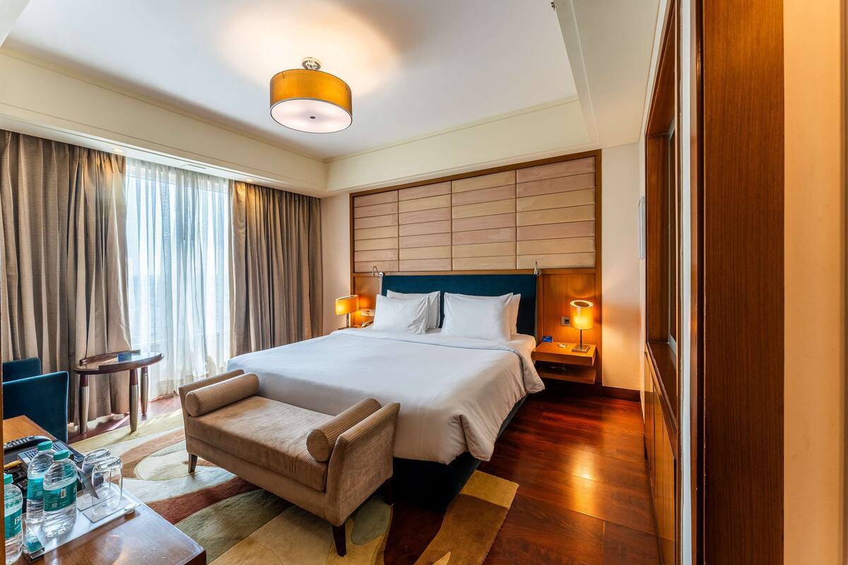 Habitación de hotel con una cama grande, lámparas de noche, un escritorio con silla y vistas a la ciudad a través de la ventana.