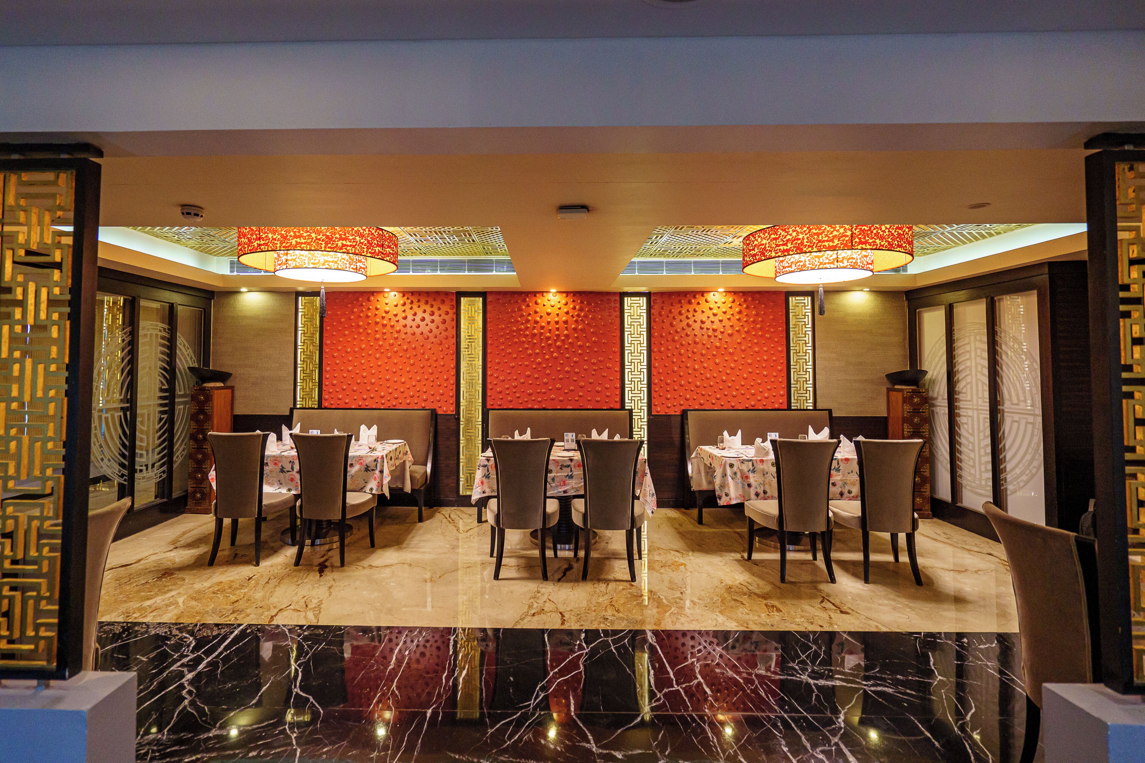 A restaurant with tables and chairs, a patterned wall, and a ceiling with hanging lights.