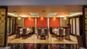 A restaurant with tables and chairs, a patterned wall, and a ceiling with hanging lights.