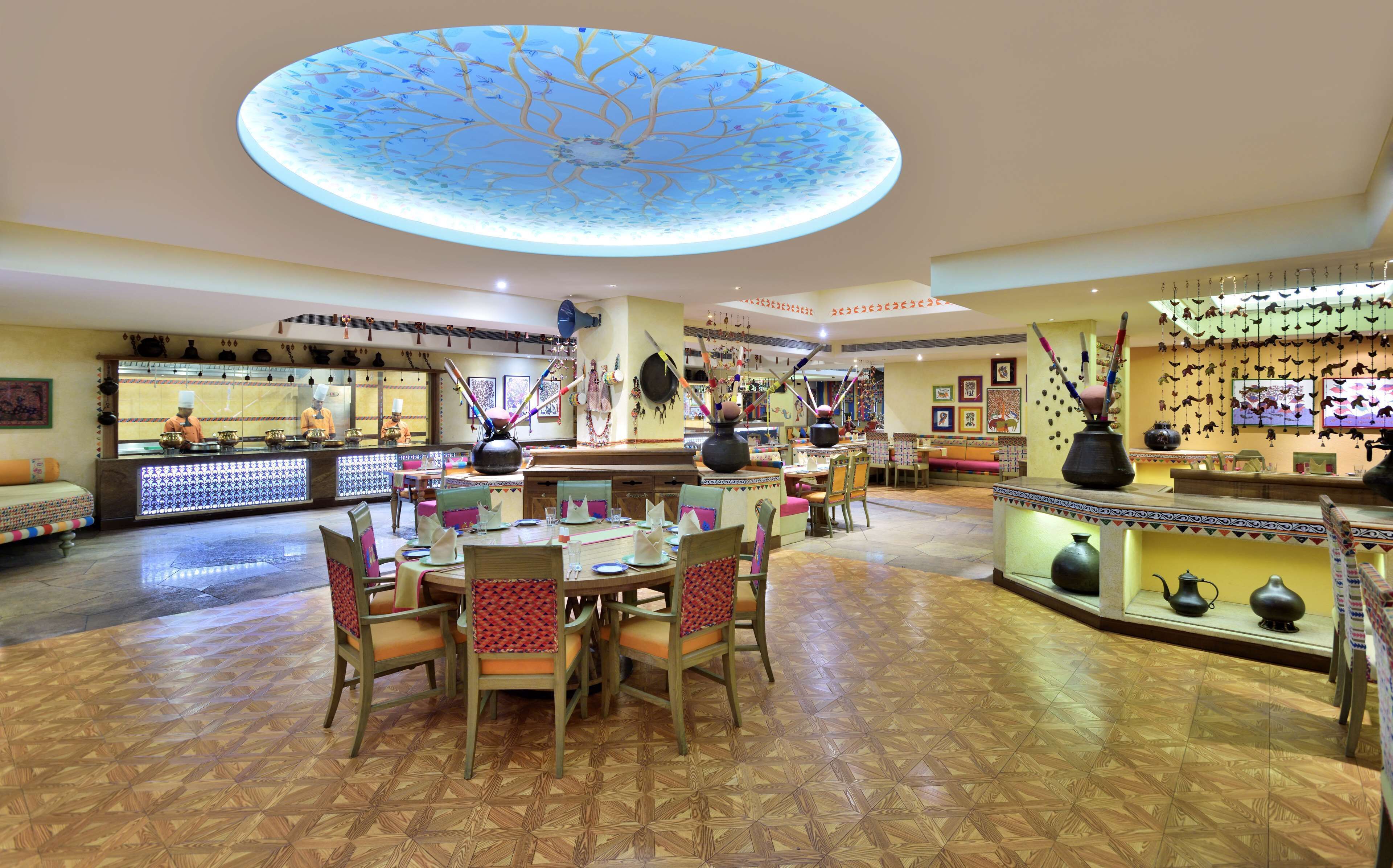 A spacious restaurant with a central dining area, a bar, and a ceiling with a tree design.