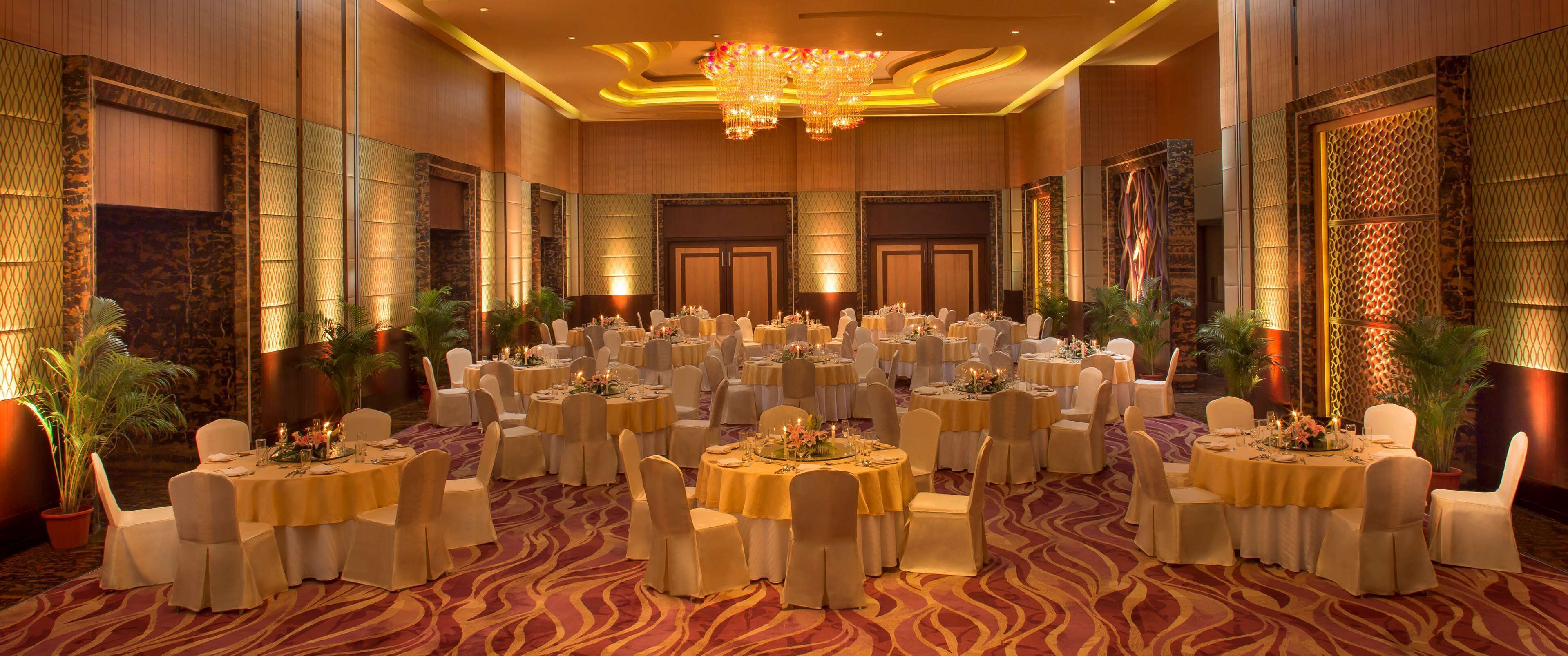A banquet hall with round tables, white chairs, and chandeliers.