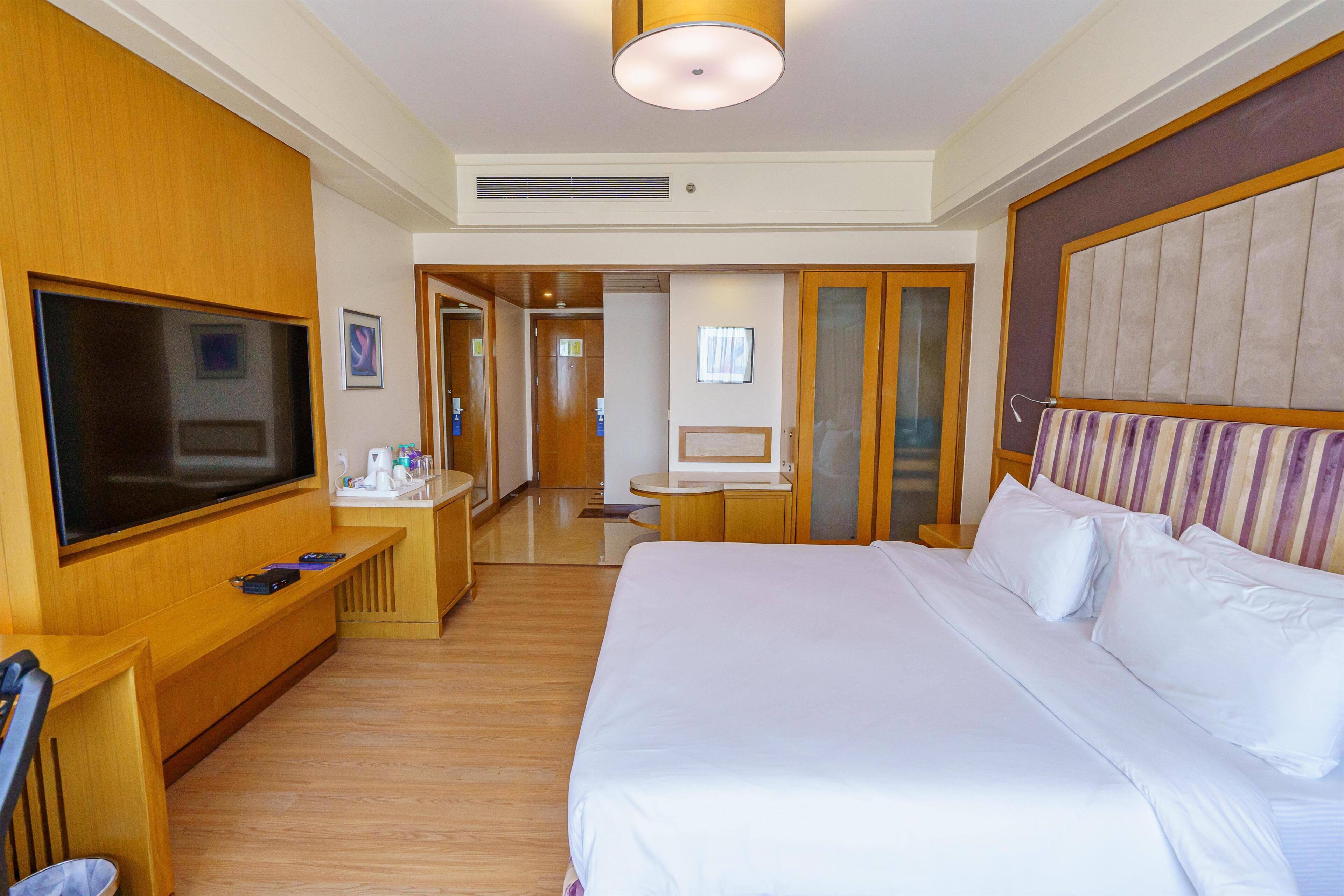 A hotel room with a large bed, a television, a desk with a chair, and a bathroom visible through an open door.