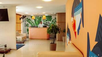 Un vestíbulo de hotel moderno con una recepción, un sofá, una mesa de centro y una planta grande en maceta.