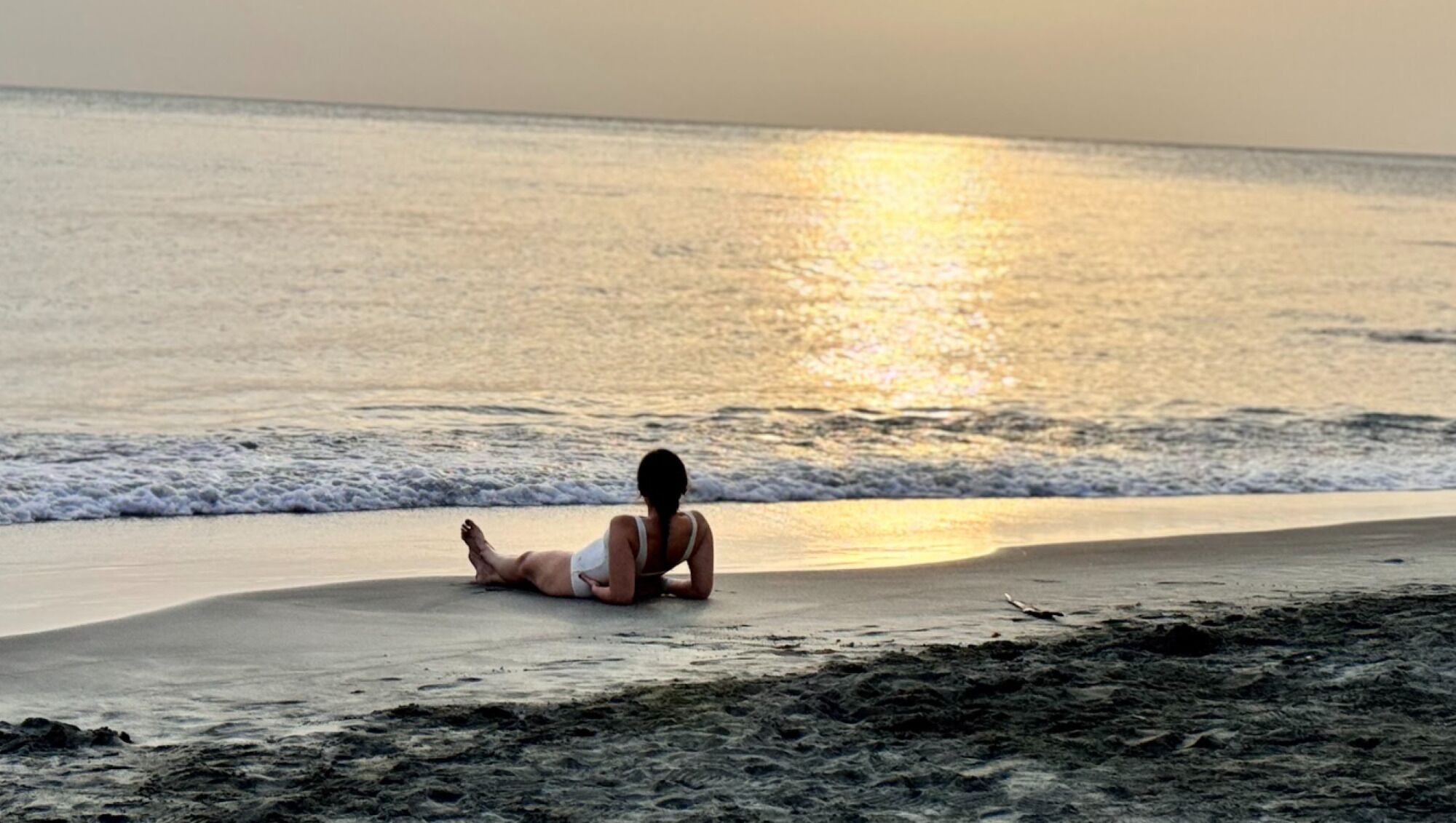Una persona recostada en la playa, con el océano al fondo.