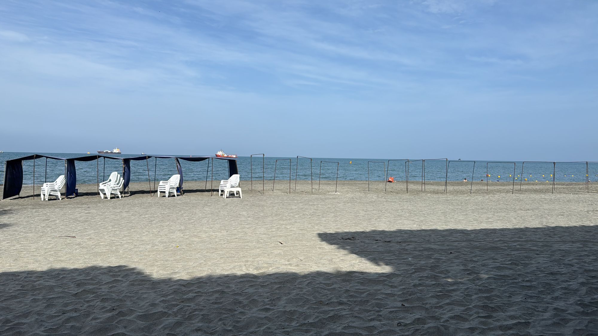 A beach with white lounge chairs under a shaded area, a sandy beach, and a calm sea.