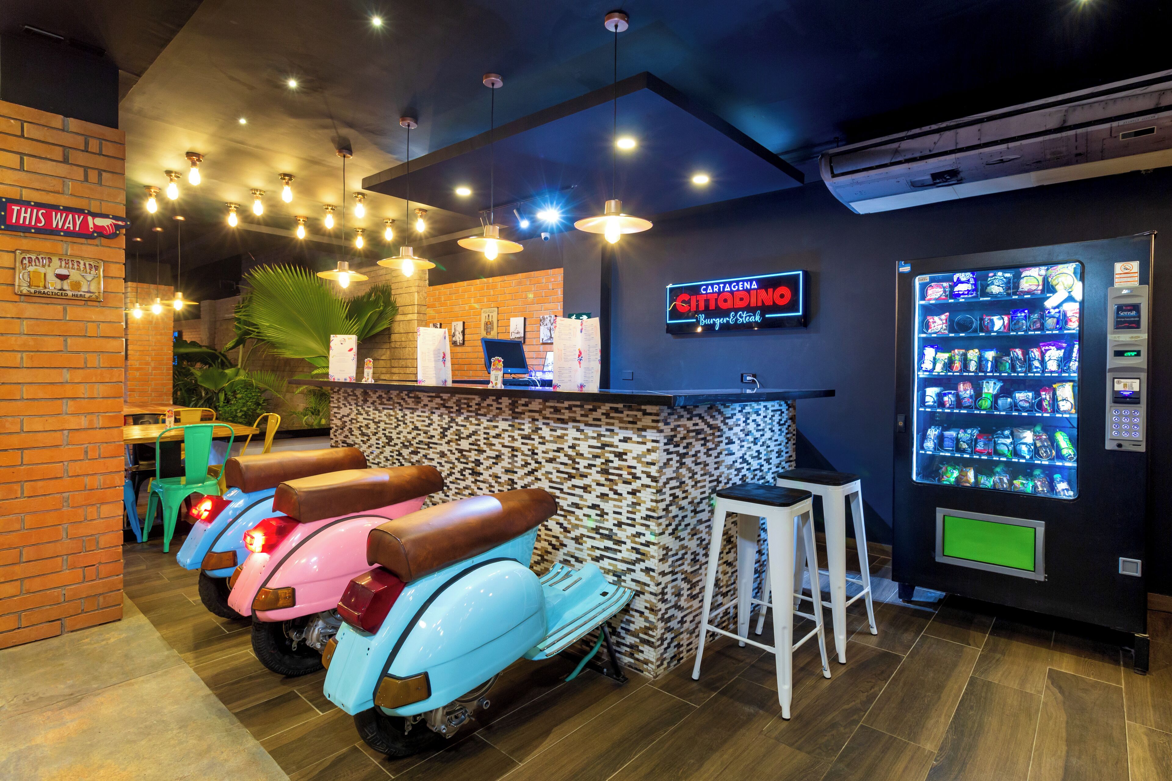 A restaurant interior with a counter, neon sign, vending machine, and scooters.