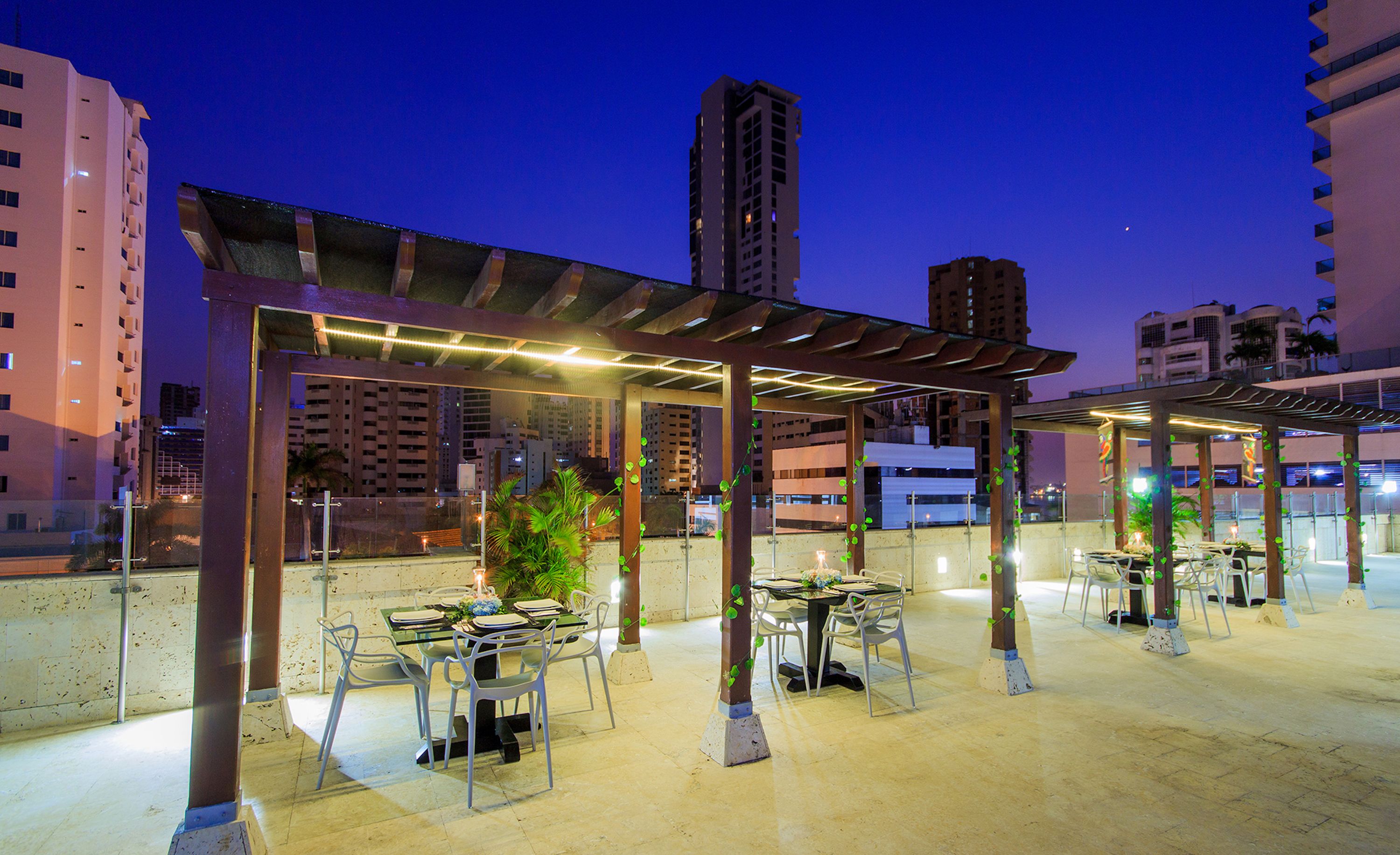 An outdoor dining area with tables and chairs, surrounded by tall buildings.