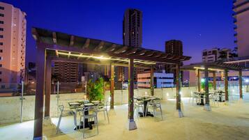 An outdoor dining area with tables and chairs, surrounded by tall buildings.