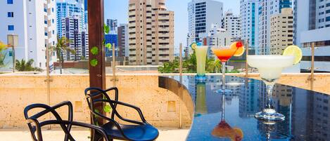 A rooftop bar with a pool table, chairs, and cocktails.