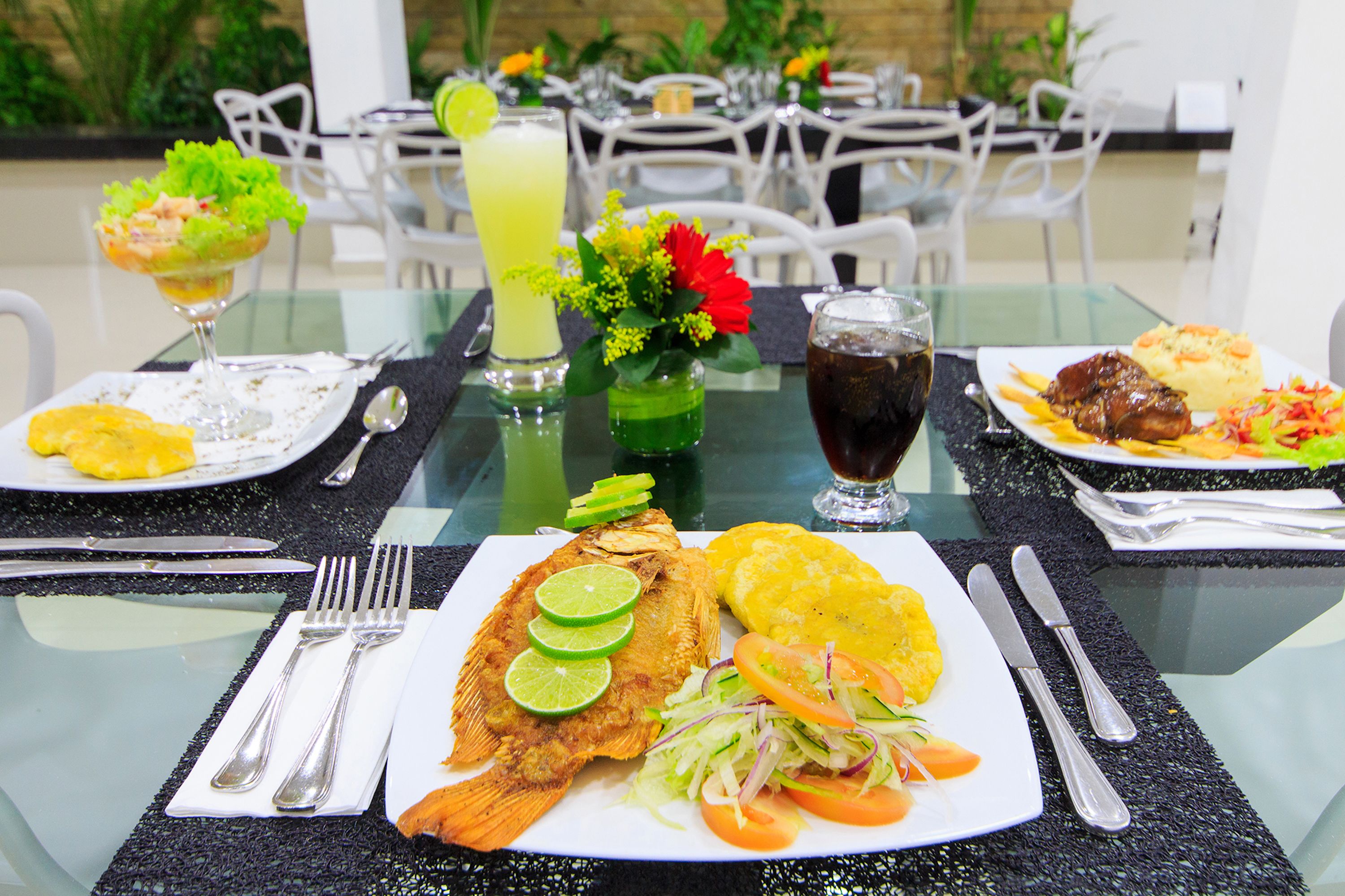 Ein Esstisch mit verschiedenen Speisen, darunter gegrillter Fisch, Salat und Kochbananen.