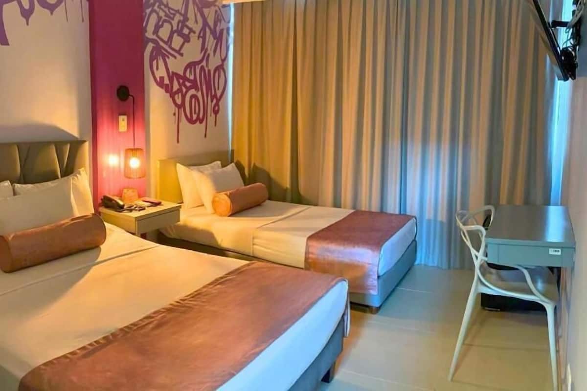 A hotel room with two beds, a desk, and a chair.