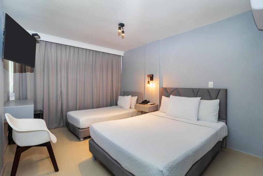 Habitación de hotel con dos camas, un escritorio, una silla, un televisor y una lámpara fijada a la pared.
