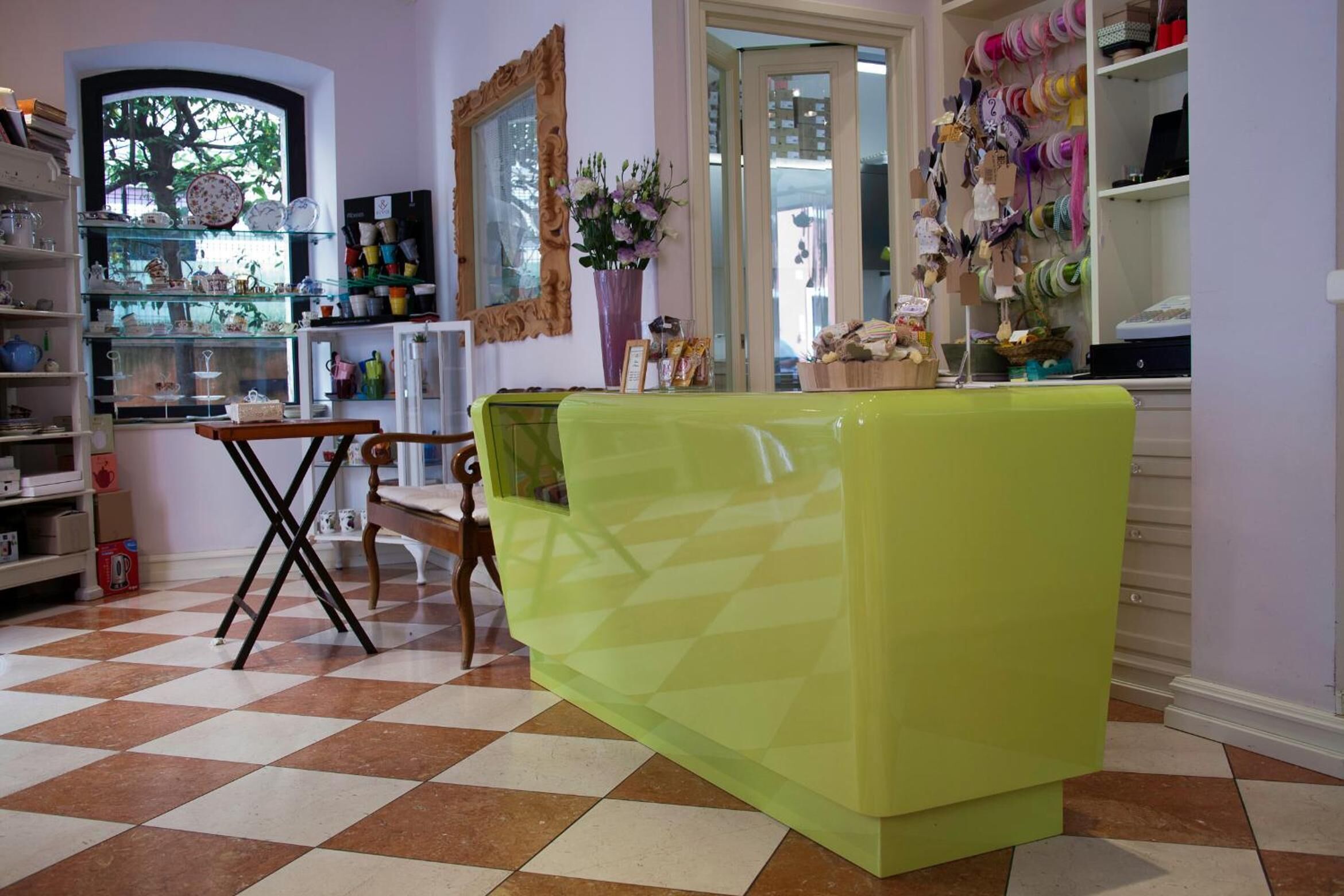 A room with a checkered floor, a green sofa, a wooden table, and shelves with various items.