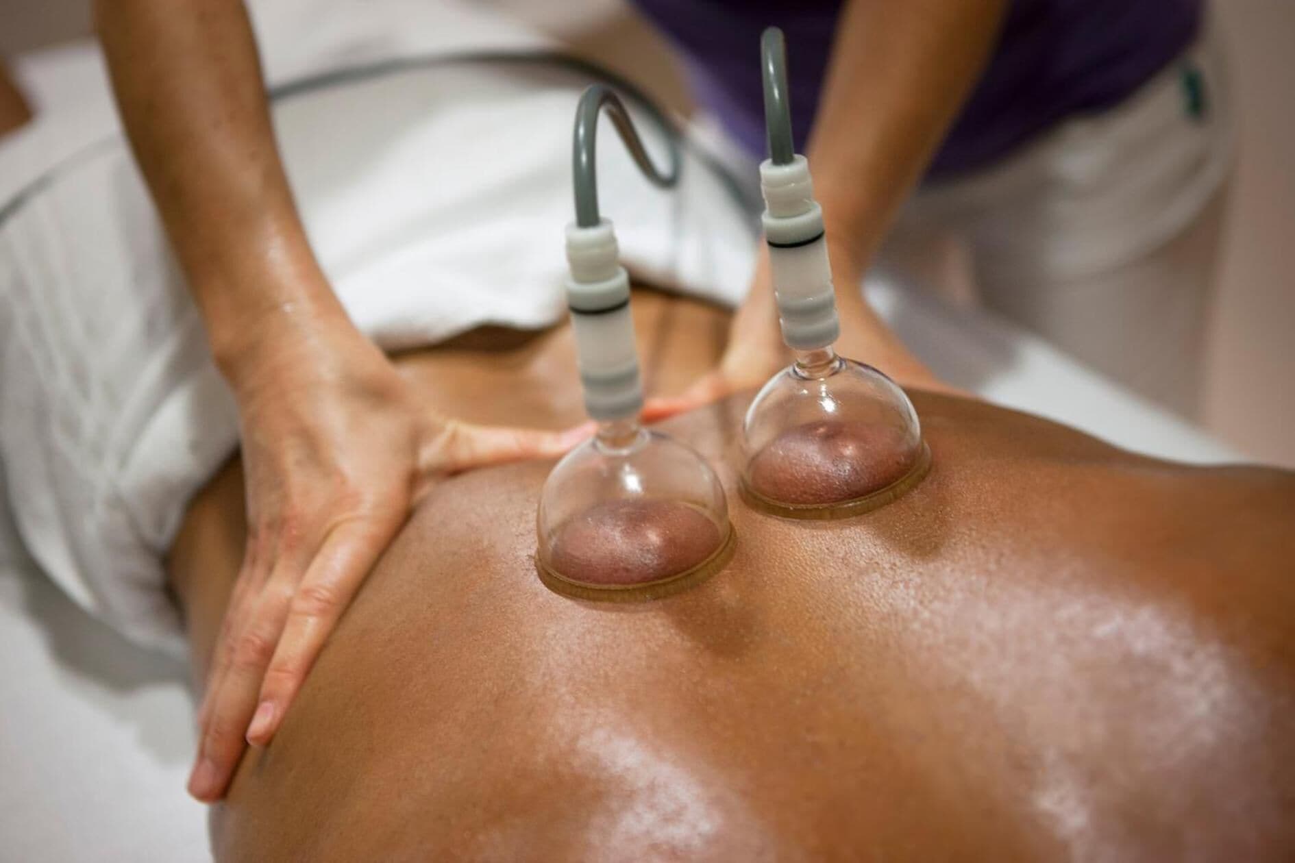 Een persoon ligt in bed met een massageapparaat op de rug.