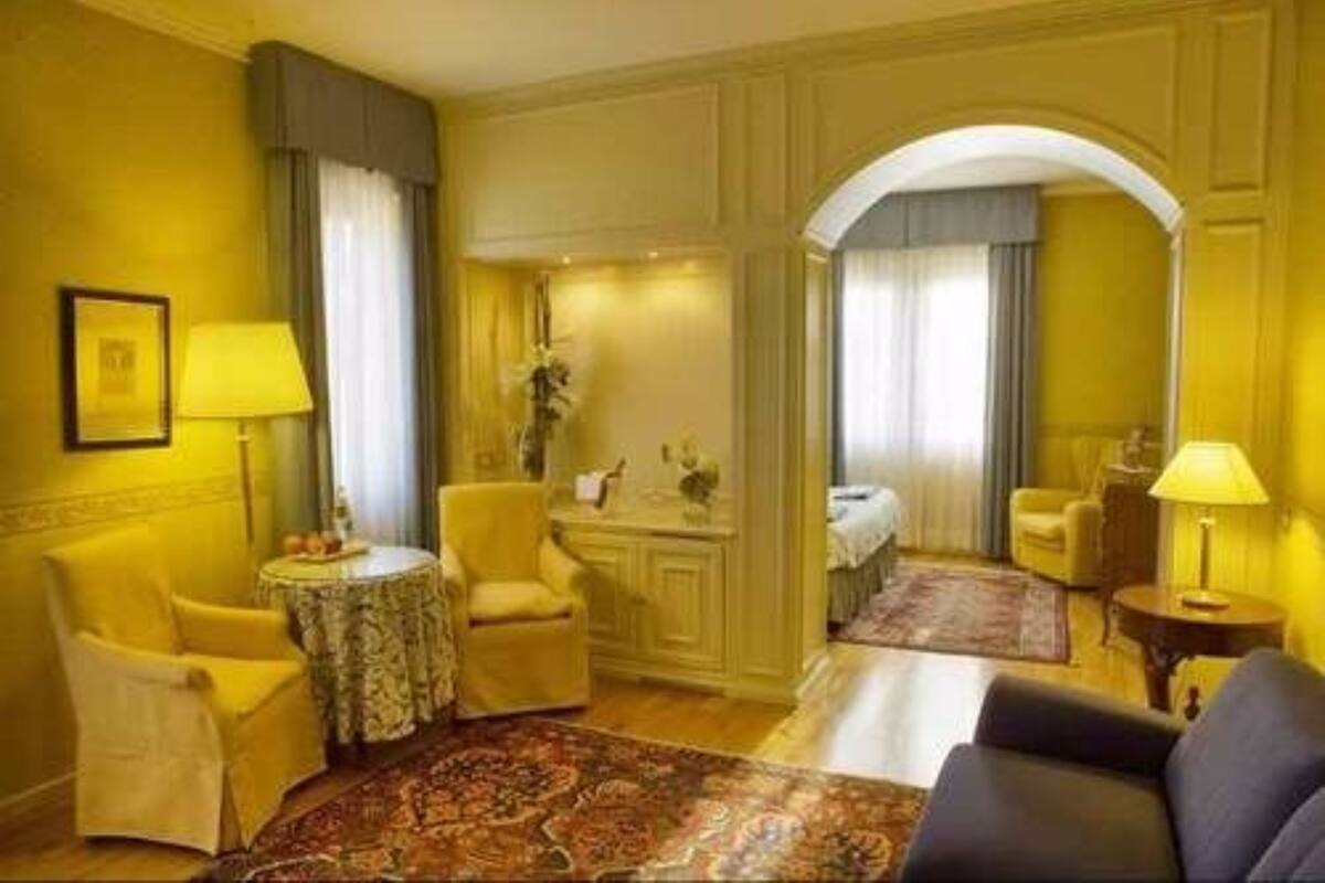 Ein Hotelzimmer mit gelber Farbgestaltung, einem runden Tisch mit Lampe, einer Couch und einem Bett.