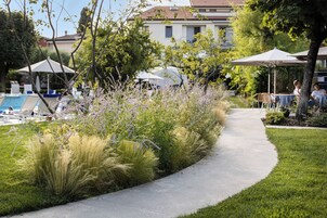 Un sentiero fiancheggiato da erba alta e fiori viola, che conduce a zone salotto all'aperto con ombrelloni.