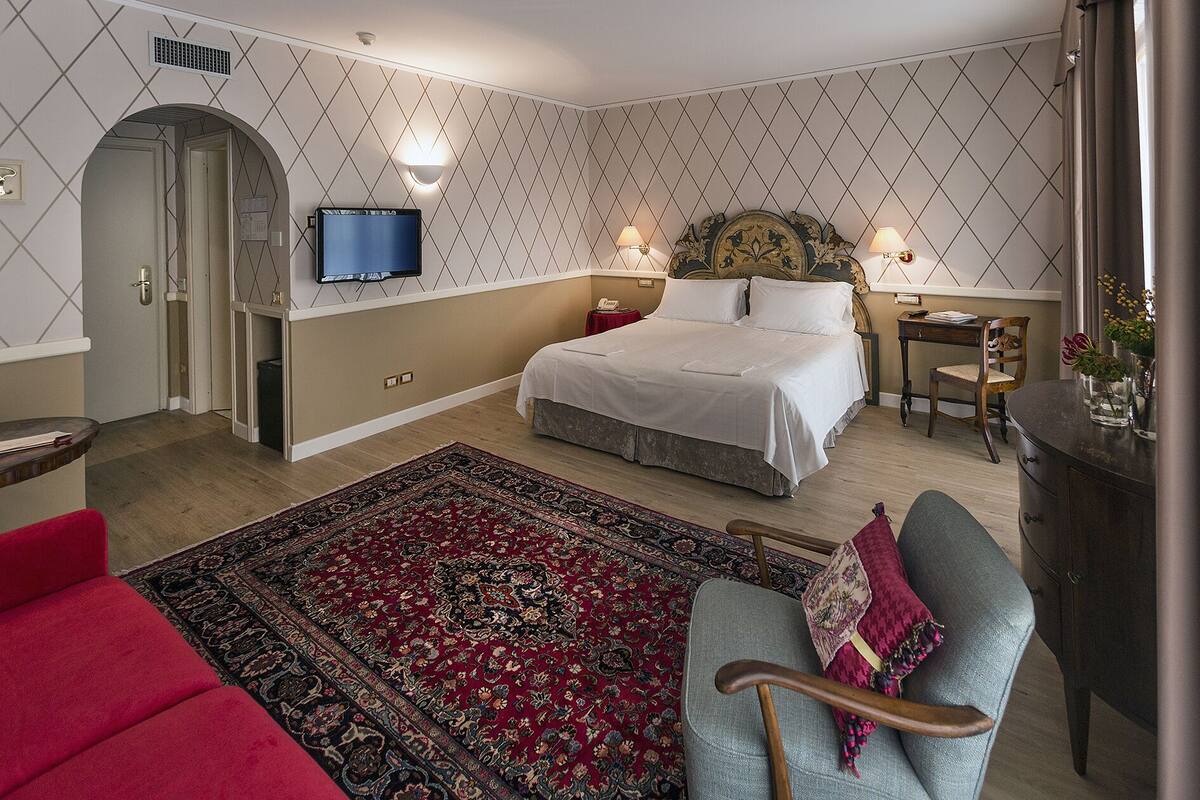 Ein Schlafzimmer mit einem Bett, einem Schreibtisch, einem Sessel, einem Fernseher und einem roten Sofa.