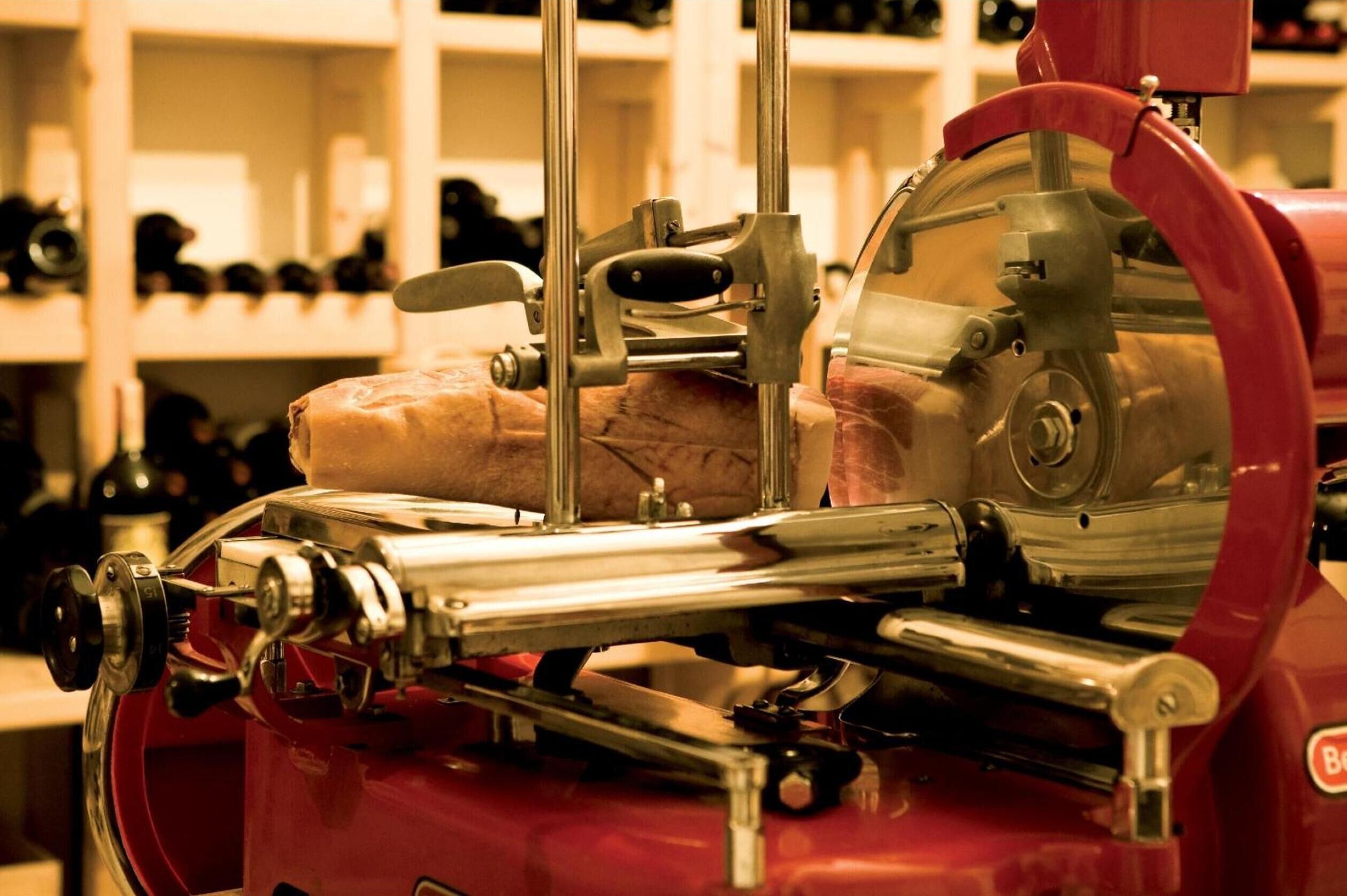 A meat slicer in a kitchen with shelves in the background.