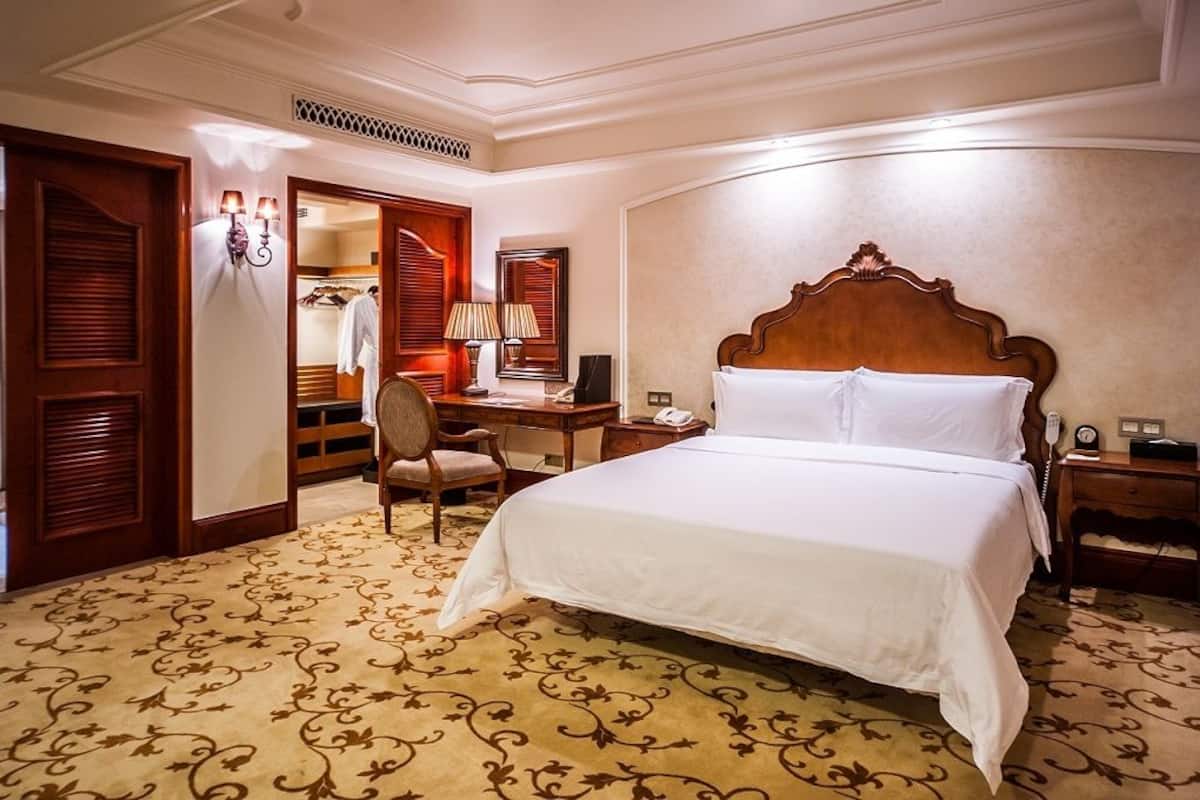 Habitación de hotel con una cama grande, un escritorio con silla, un armario y un espejo.
