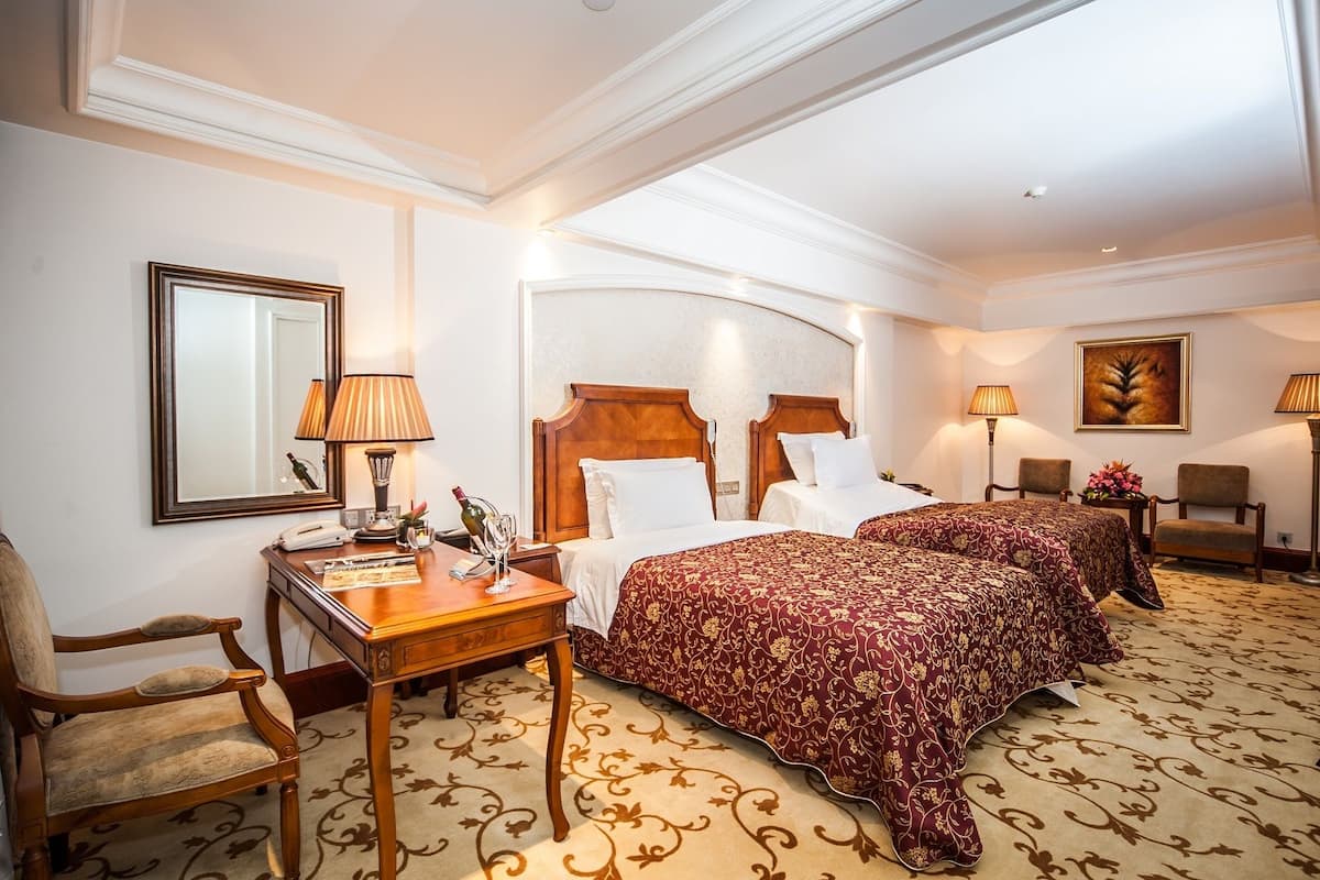 Habitación de hotel con dos camas, un escritorio, una silla, un espejo y un cuadro en la pared.
