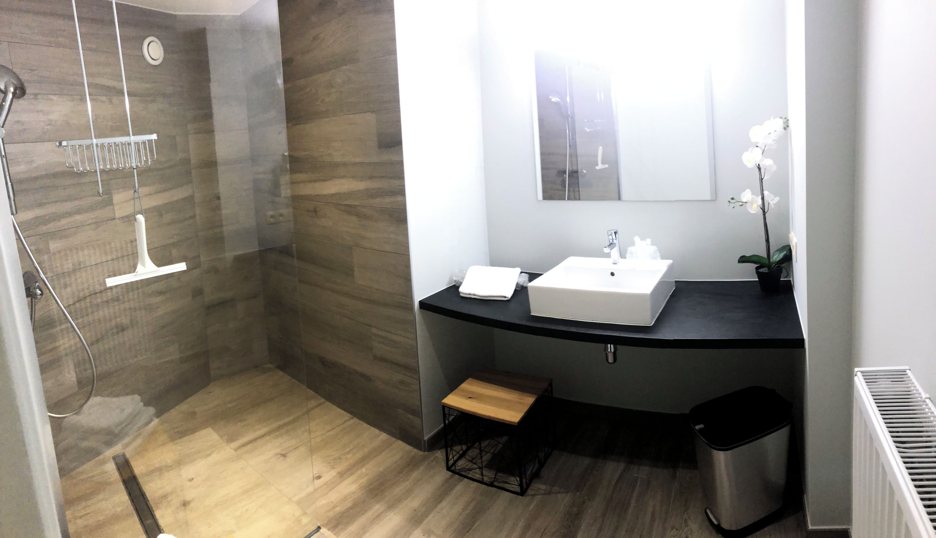 Un baño moderno con ducha, lavamanos y un taburete de madera.