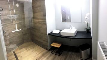 Un baño moderno con ducha, lavamanos y un taburete de madera.