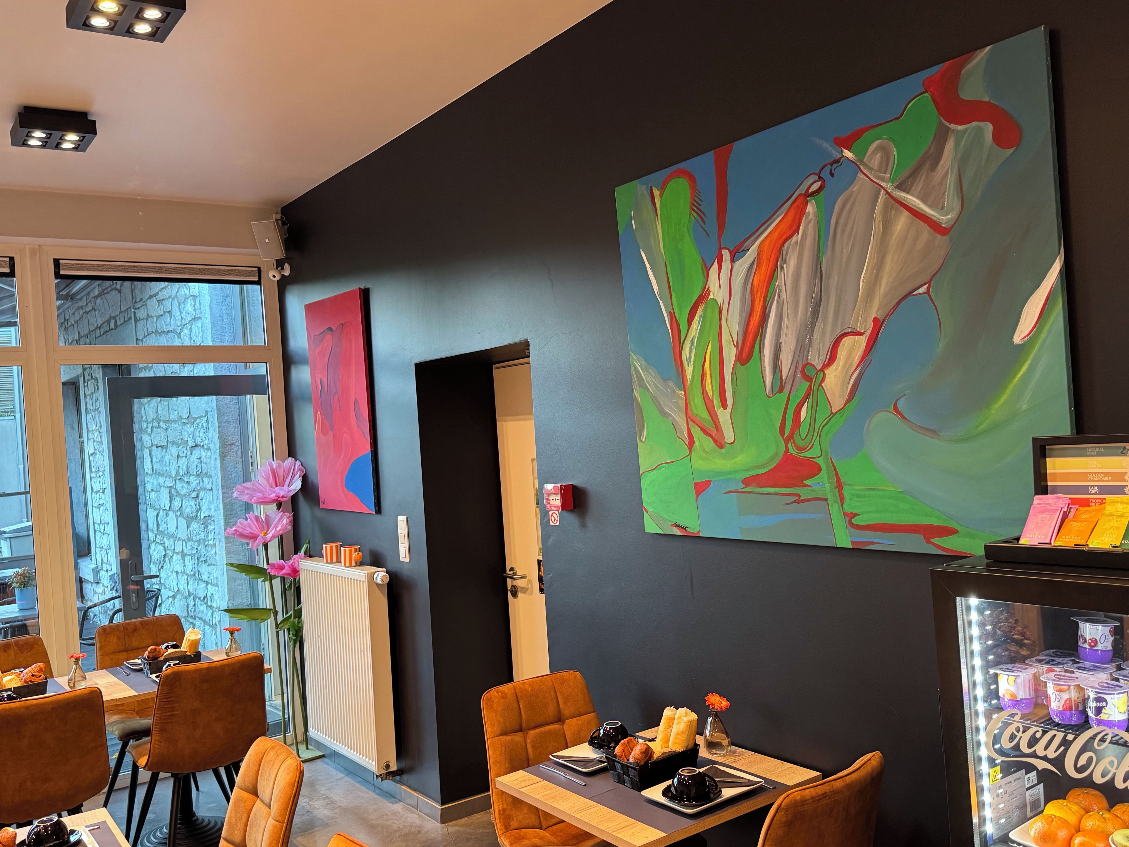 Un espace de repas moderne agrémenté d’un grand tableau abstrait, d’une machine à café en verre et offrant une vue sur l’extérieur.